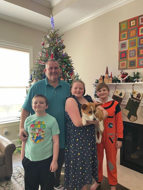Sean Willson and his three children and dog standing in front of a Christmas tree.